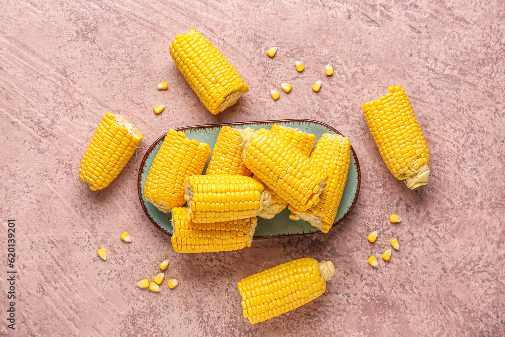 Plate with cut fresh corn cobs and seeds on pink background