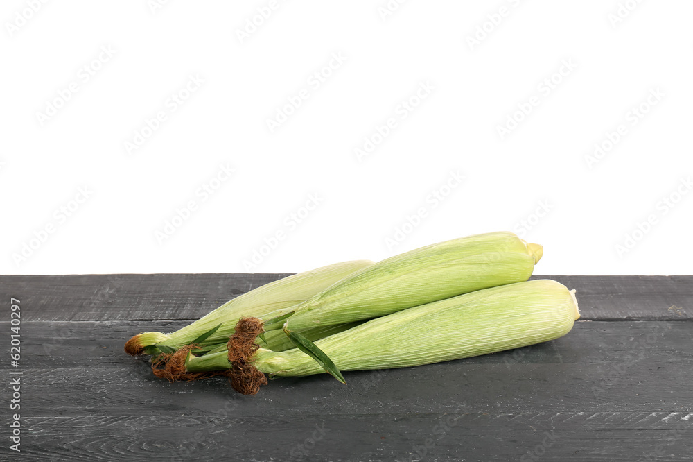 Fresh corn cobs on black wooden table against white background