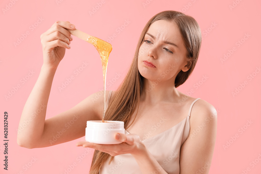 Displeased young woman with sugaring paste on pink background