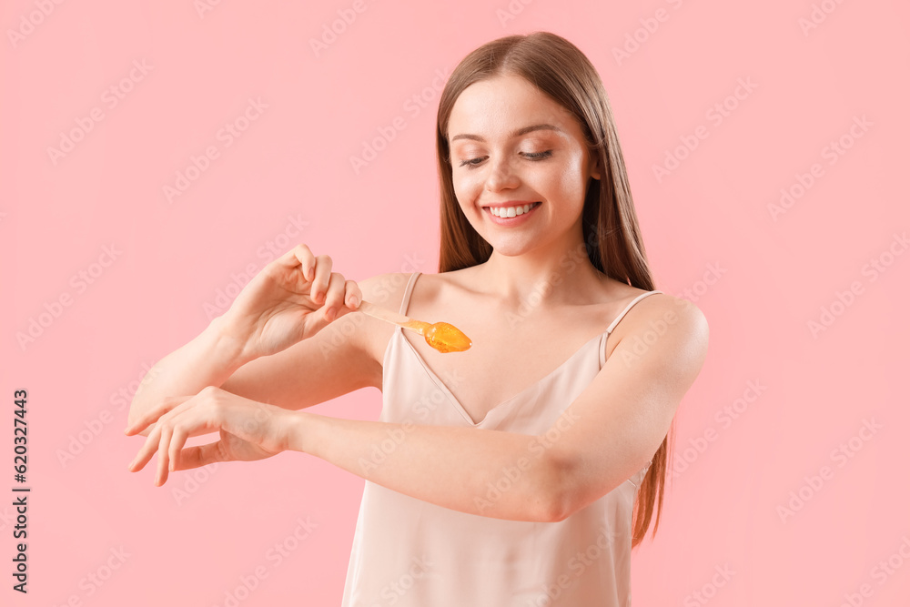 Young woman applying sugaring paste onto her arm against pink background