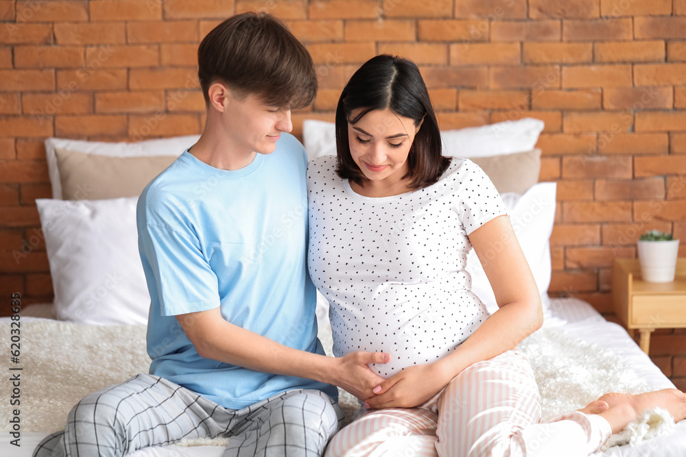 Young pregnant couple sitting in bedroom