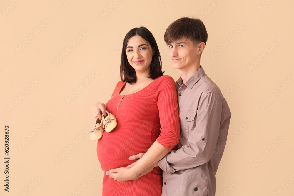 Young pregnant couple with baby booties on beige background