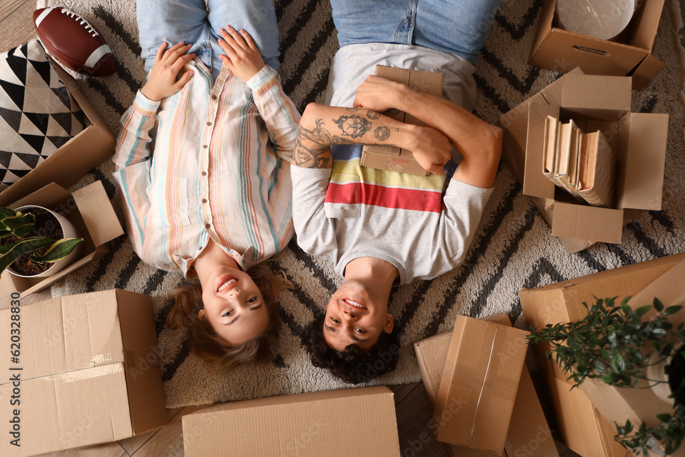 Young couple with moving boxes lying on carpet, top view