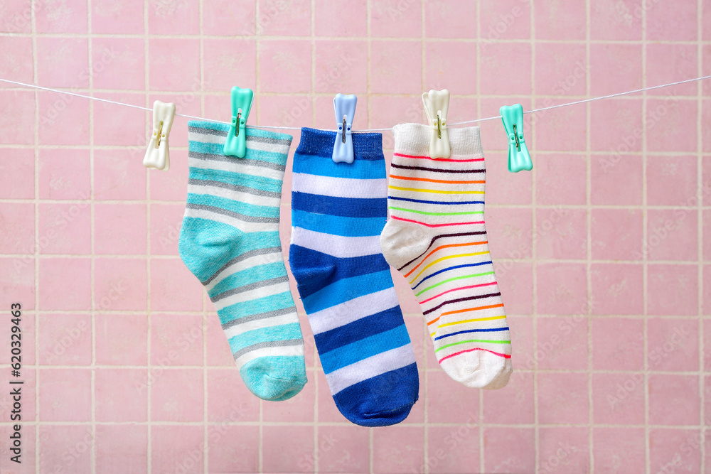 Different socks hanging on rope against color tile background