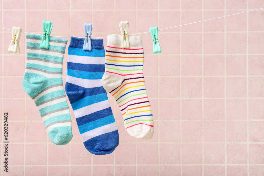 Different socks hanging on rope against color tile background