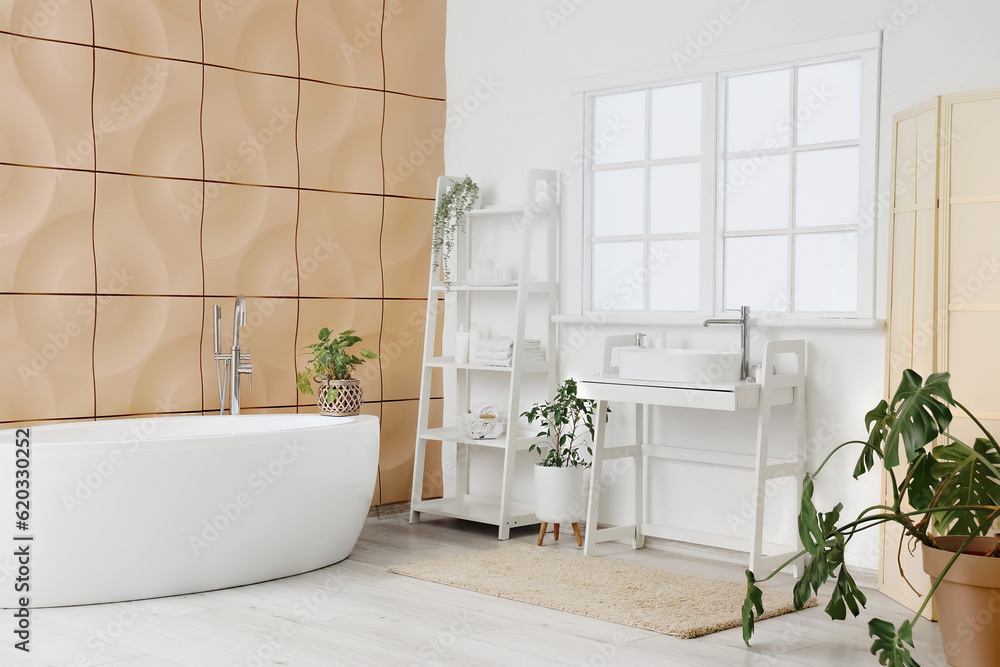 Interior of light bathroom with sink, bathtub, shelving unit and houseplants