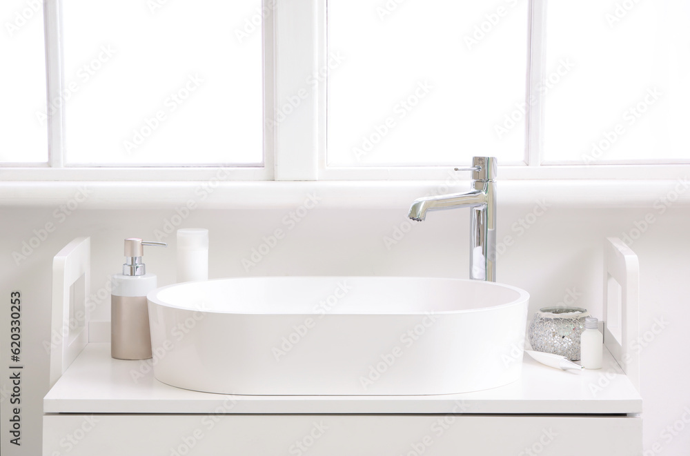 White sink with bath accessories on table in light bathroom