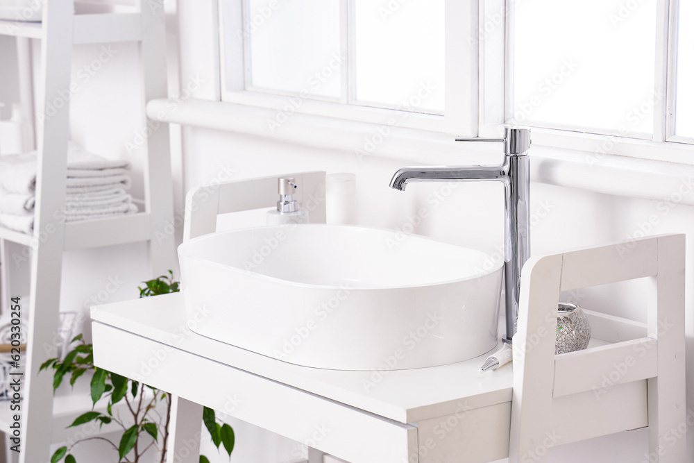 White sink with bath accessories on table in light bathroom