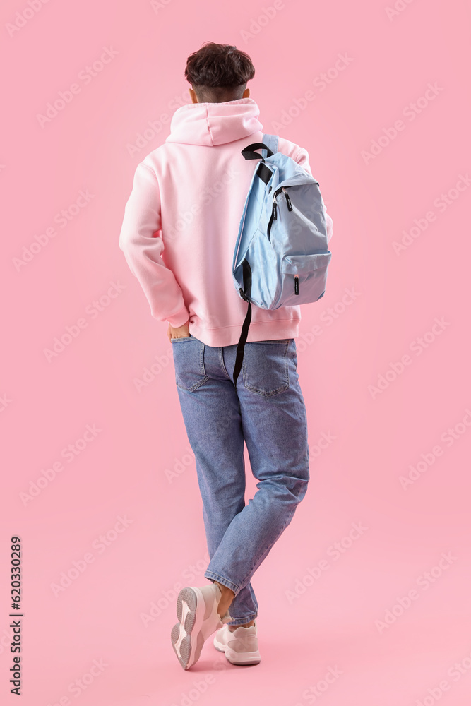 Male student with backpack on pink background, back view