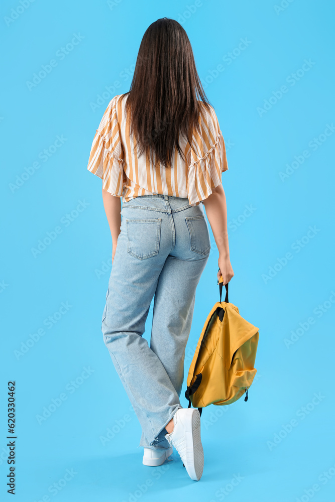 Female student with backpack on blue background, back view