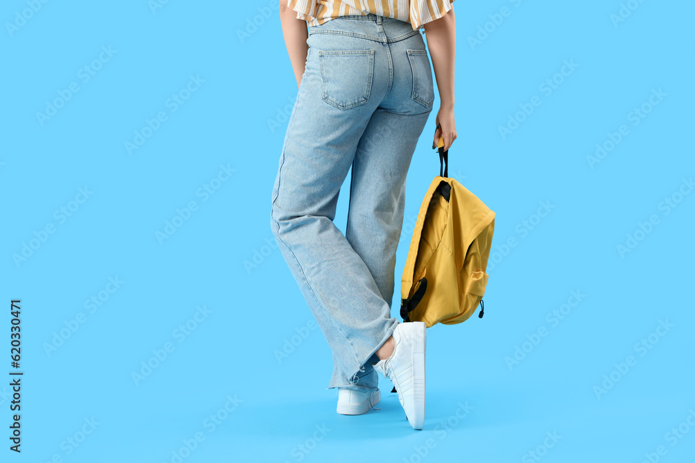 Female student with backpack on blue background, back view