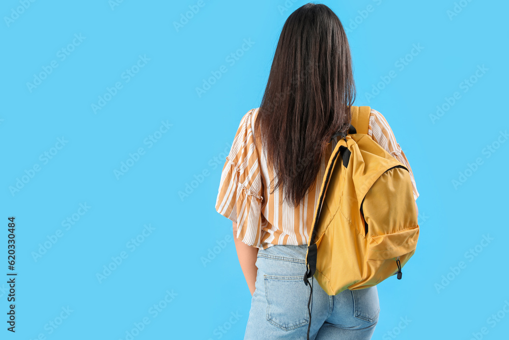 Female student with backpack on blue background, back view