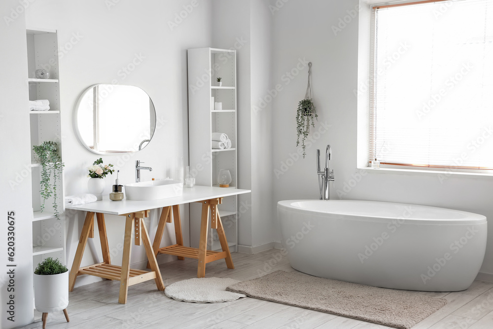 Interior of light bathroom with white sink, shelving units and bathtub