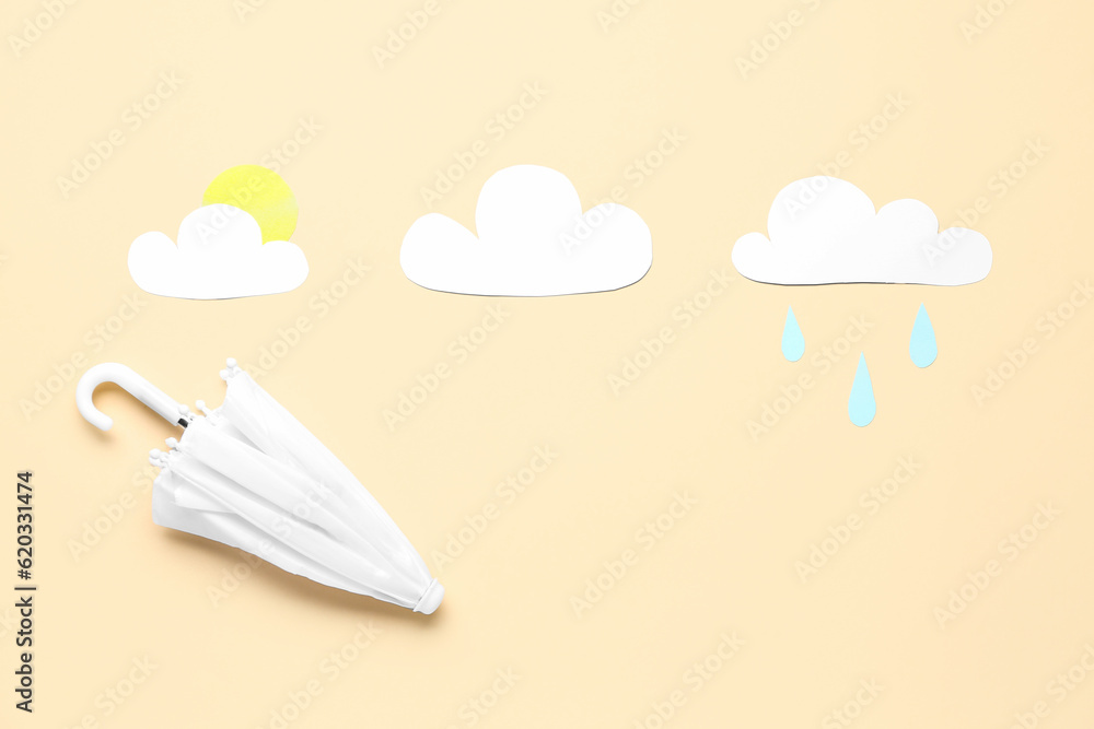 Umbrella with paper clouds, sun and drops on beige background. Weather forecast concept