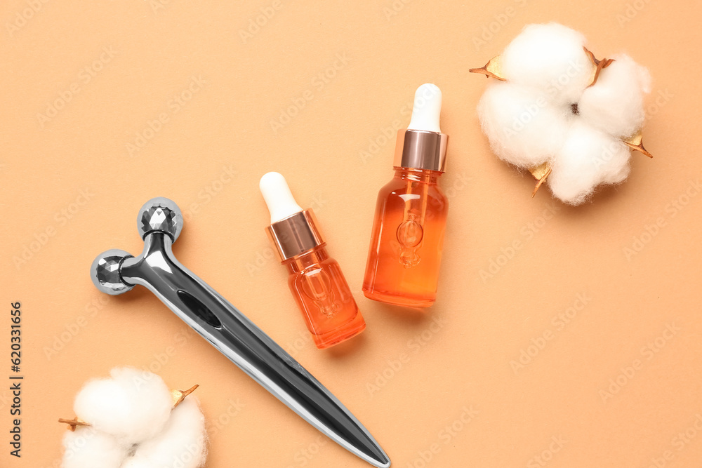 Bottles of essential oil, facial massage tool and cotton flowers on color background