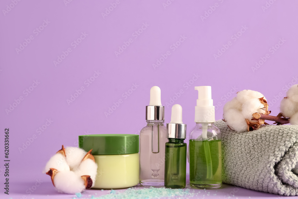 Cosmetic products, clean towel and cotton flowers on lilac background, closeup