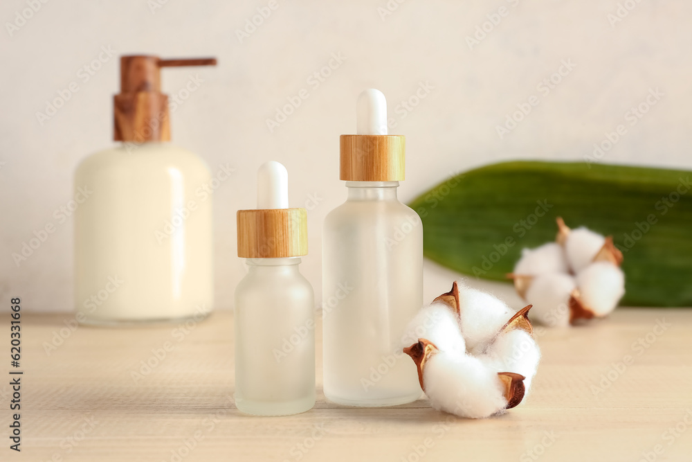 Bottles of essential oil and cotton flowers on wooden background