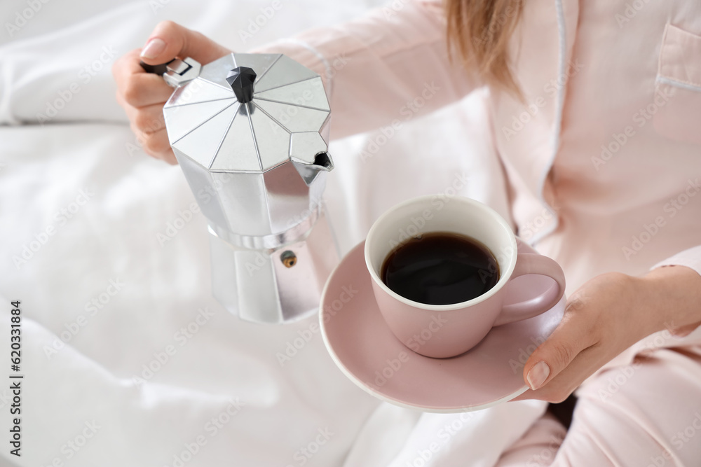 Woman holding geyser coffee maker and cup of espresso in bed