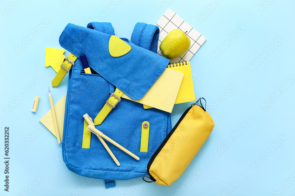 Color school backpack with pencil case, notebooks and apple on blue background