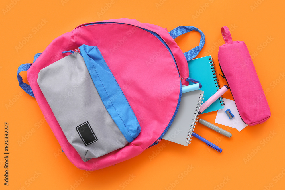 Pink school backpack with pencil case, notebooks and markers on orange background