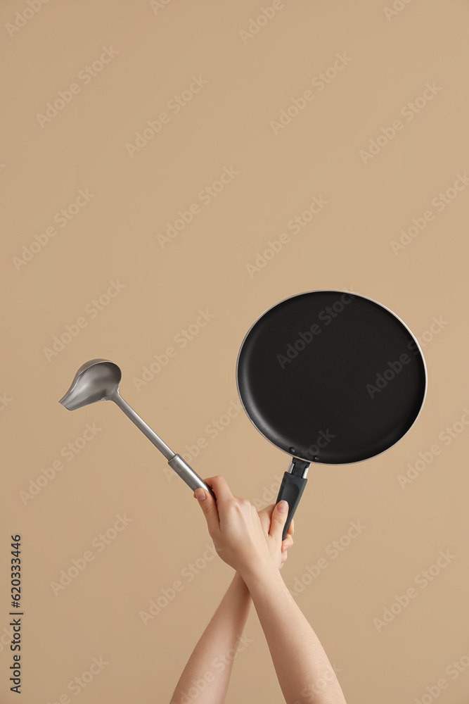 Female hands holding frying pan and ladle on brown background