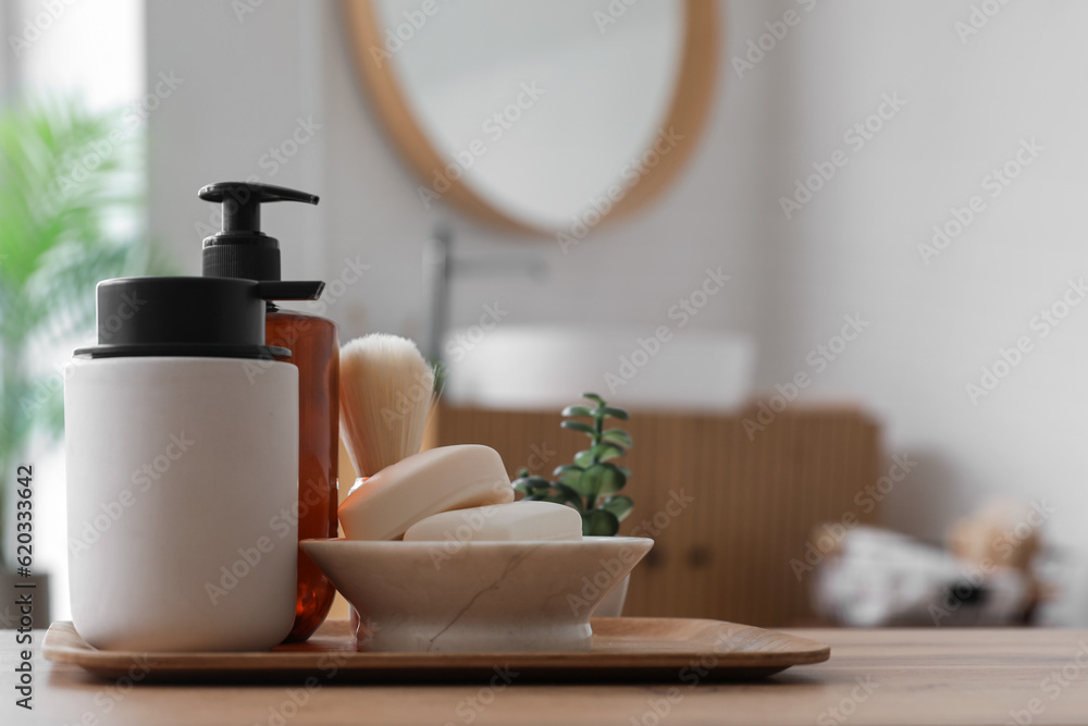 Soap bars, dispensers and shaving brush on wooden table in bathroom