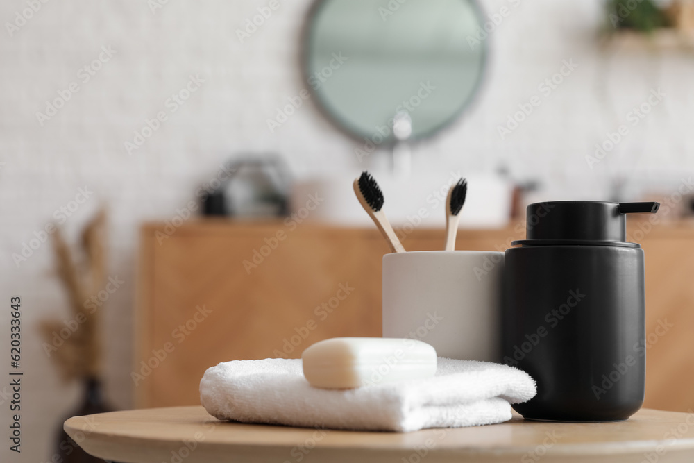 Bar of soap, dispenser, towel and cup with toothbrushes on table in bathroom, closeup