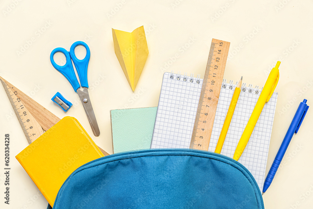 School backpack with paper plane and different stationery on light background