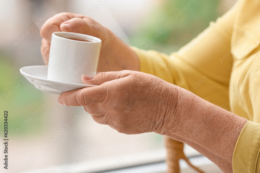 Senior woman with cup of coffee at home, closeup