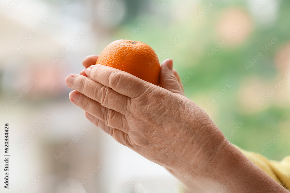 Senior woman with orange at home, closeup