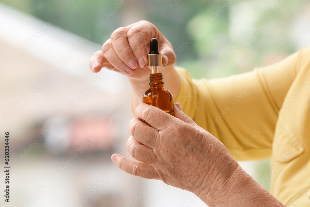 Senior woman with cosmetic dropper bottle at home, closeup