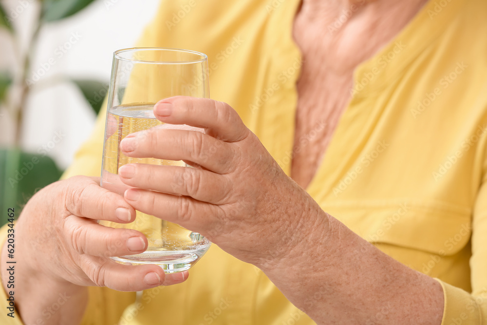 Senior woman with glass of water at home, closeup