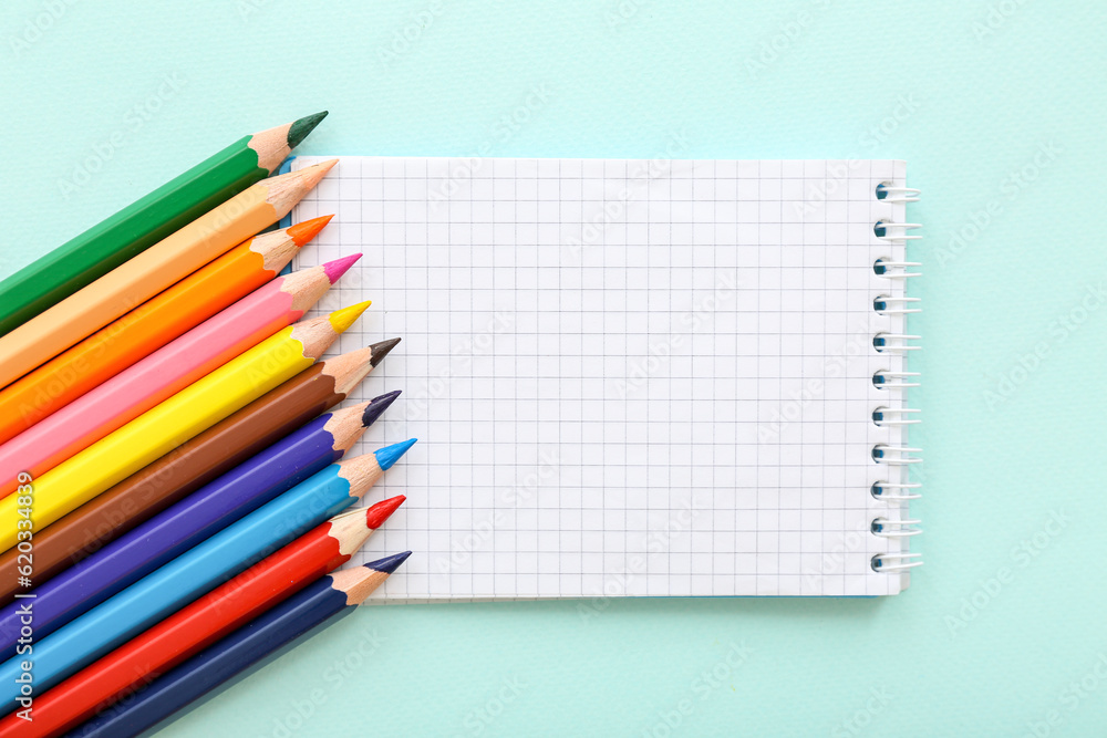 Blank notebook with different colorful pencils on blue background