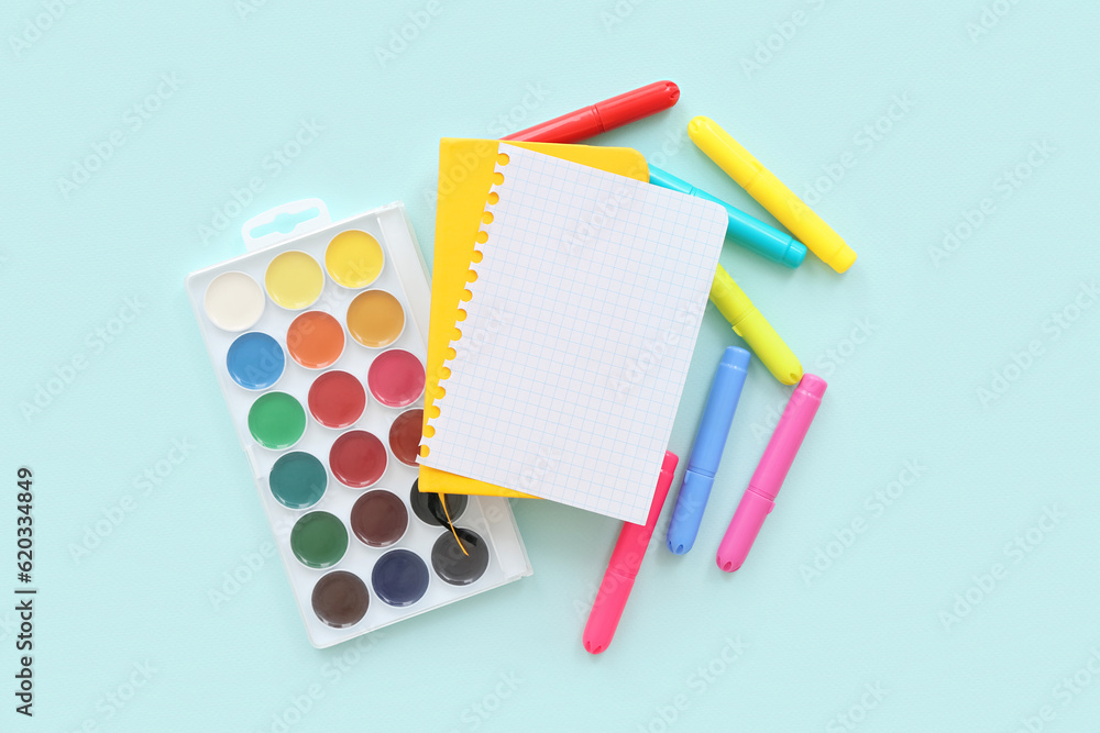 Blank notebook with different colorful markers and paints on blue background