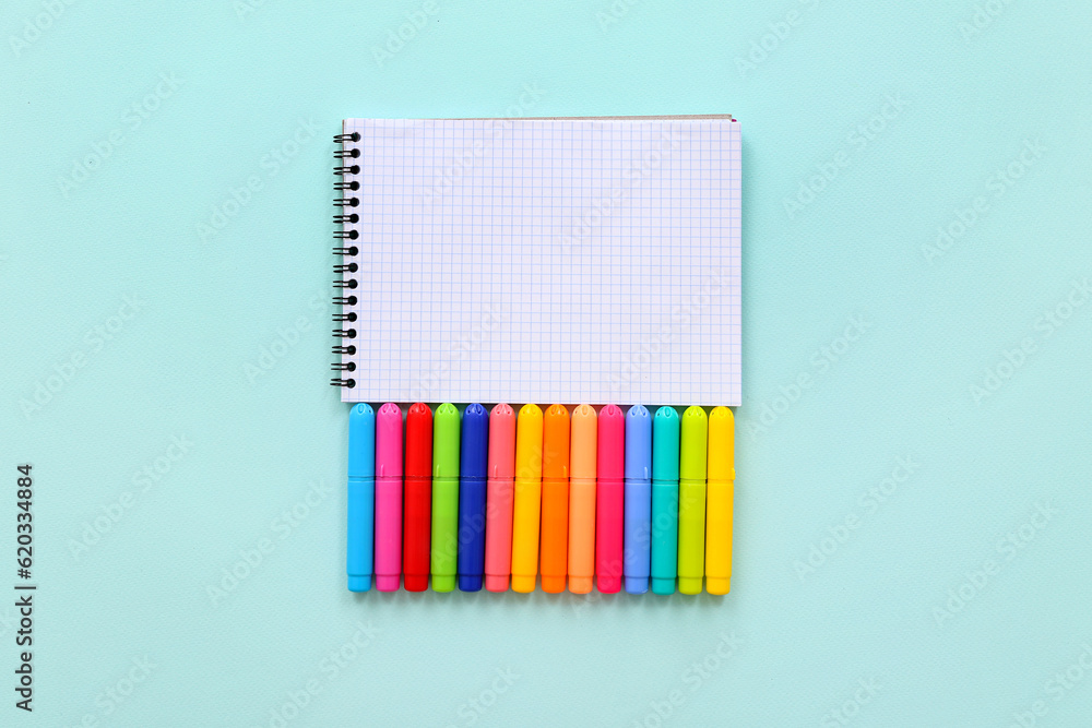 Blank notebook with different colorful markers on blue background