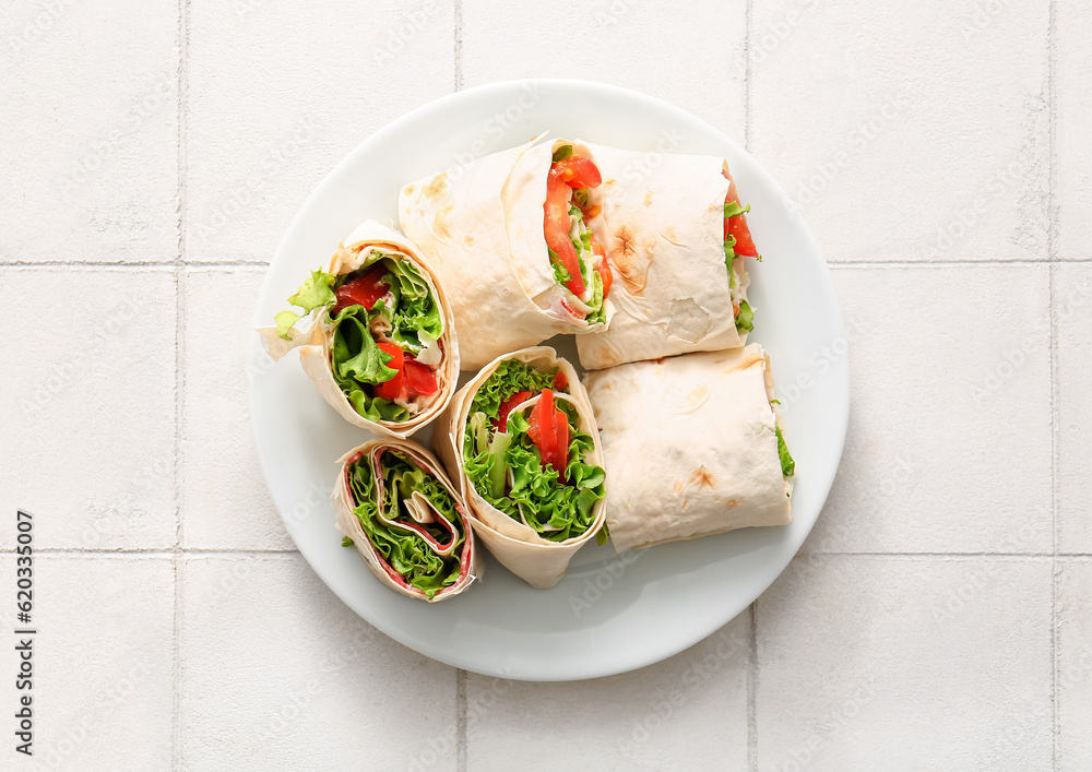 Plate of tasty lavash rolls with tomatoes and greens on white tile background