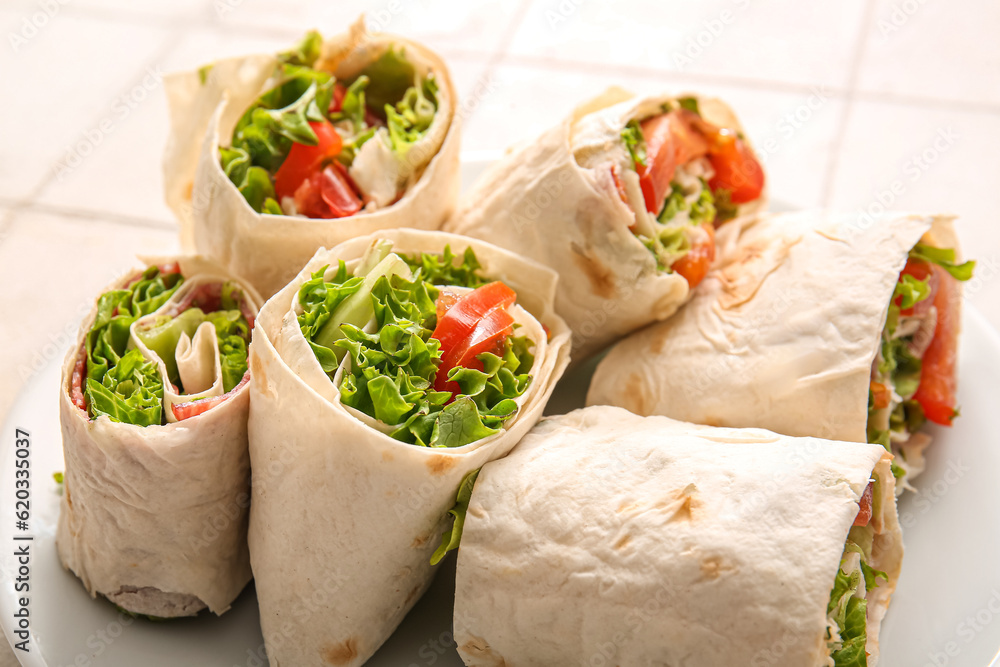 Plate of tasty lavash rolls with tomatoes and greens on white tile background