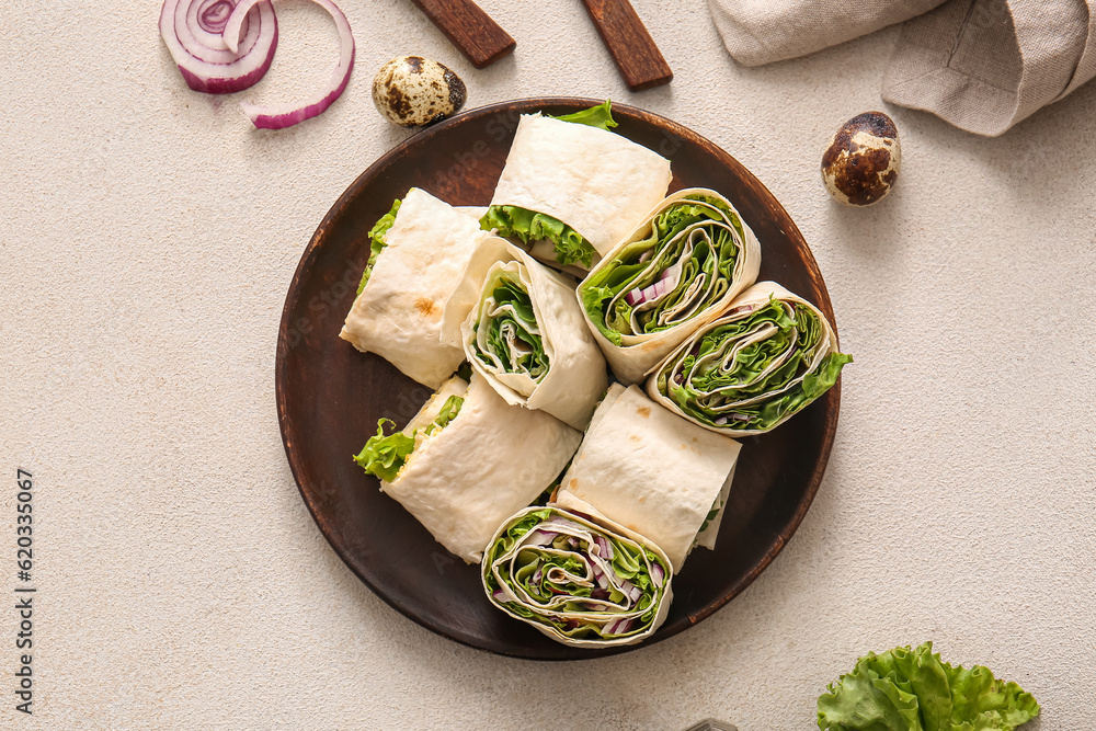 Plate of tasty lavash rolls with onion and greens on light background