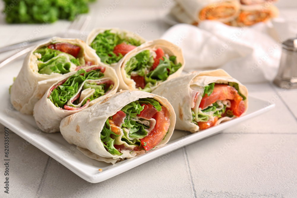 Plate of tasty lavash rolls with tomatoes and greens on white tile background