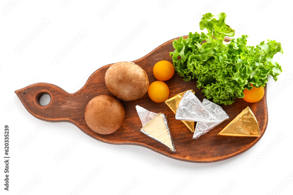 Board with triangles of tasty processed cheese in foil and vegetables on white background