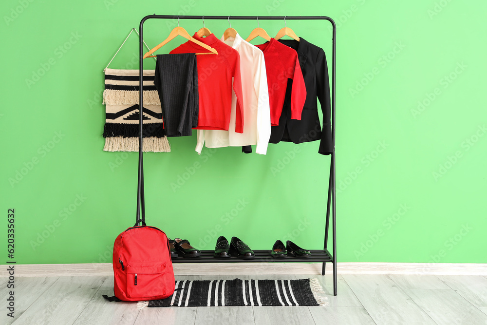 Stylish school uniform hanging on rack, backpack and shoes near green wall in room