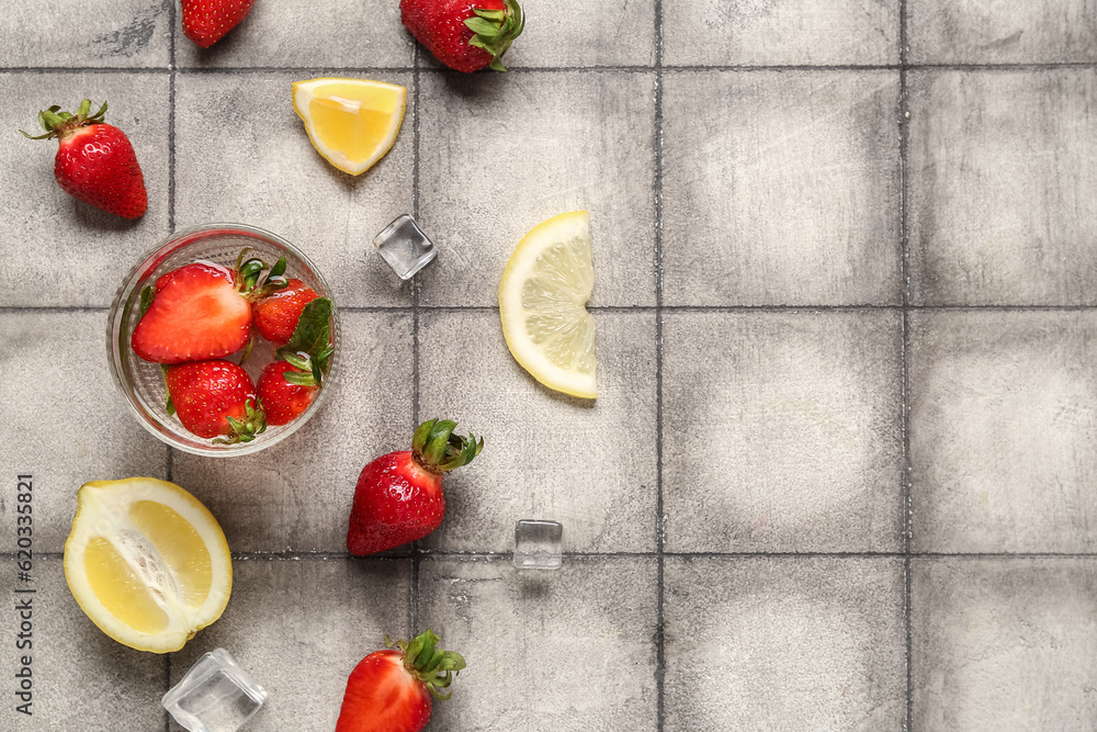 Glass of fresh lemonade with strawberry and lemon on grey tile background