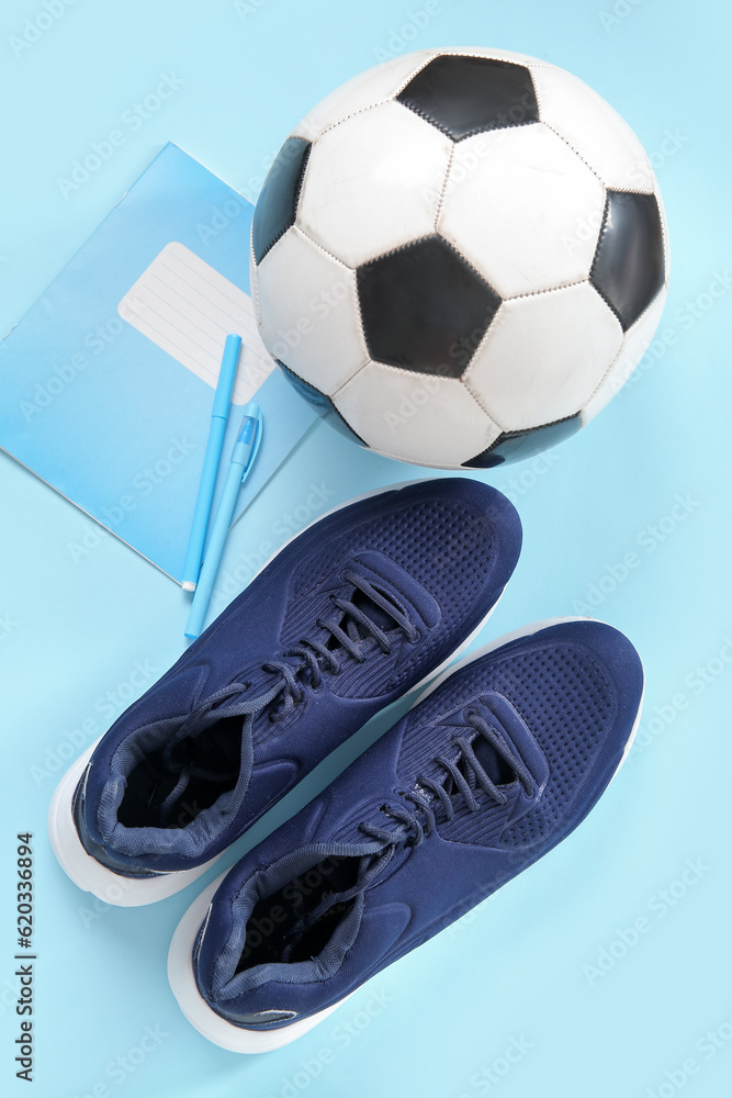 Sneakers with soccer ball, notebook and pens on blue background