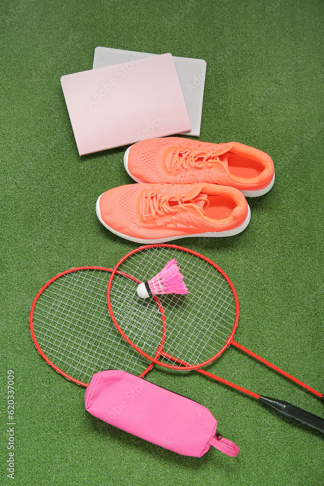 Sneakers with rackets, badminton shuttlecock and stationery on color background