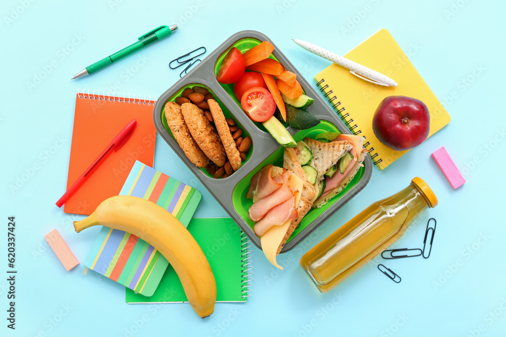 Stationery, drink and lunch box with tasty food on blue background