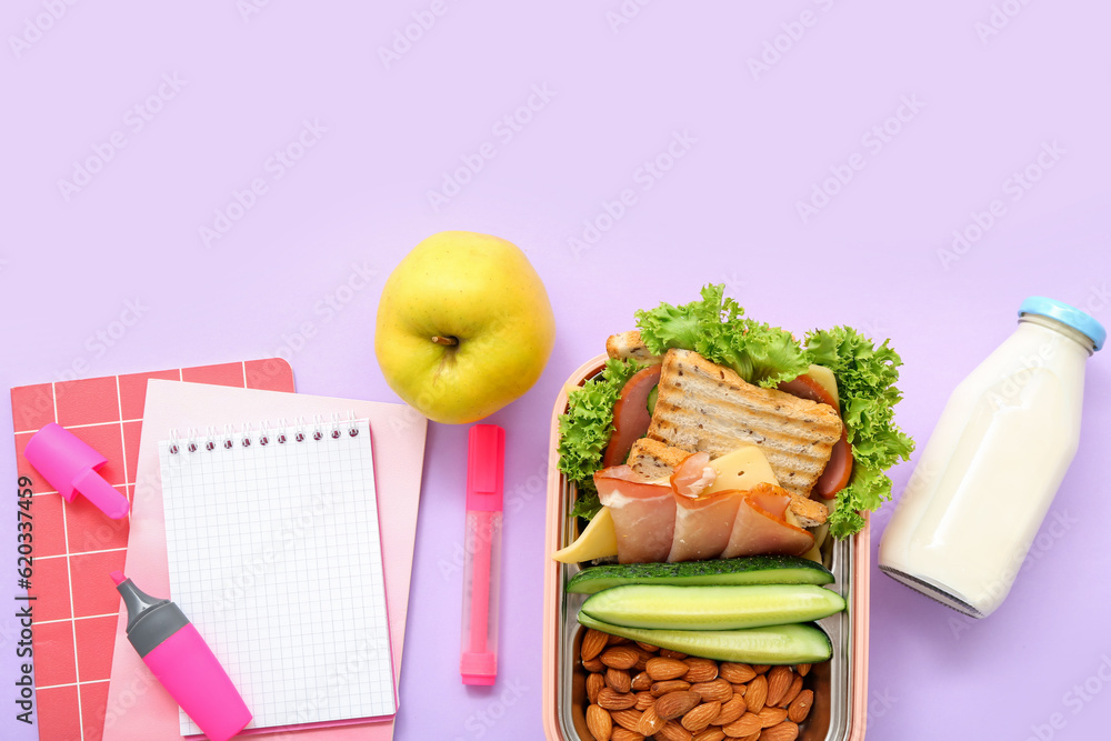 Stationery, drink and lunch box with tasty food on lilac background