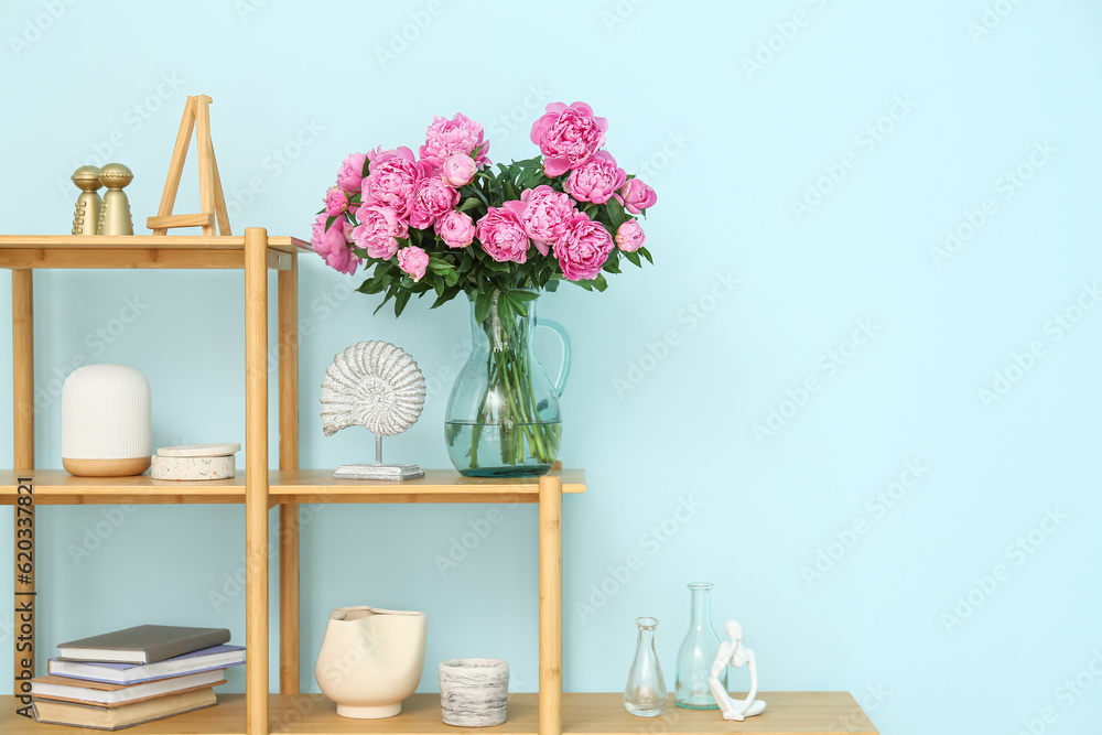 Vase of pink peonies on shelving unit near blue wall