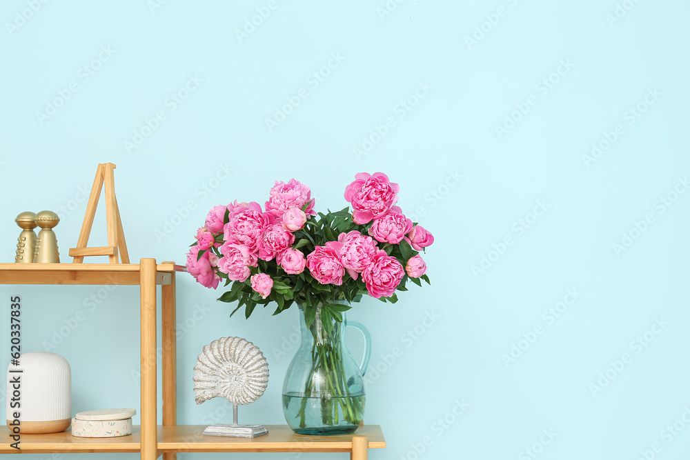 Vase of pink peonies on shelving unit near blue wall