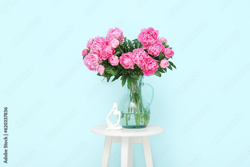 Vase of pink peonies with figurine on chair near blue wall