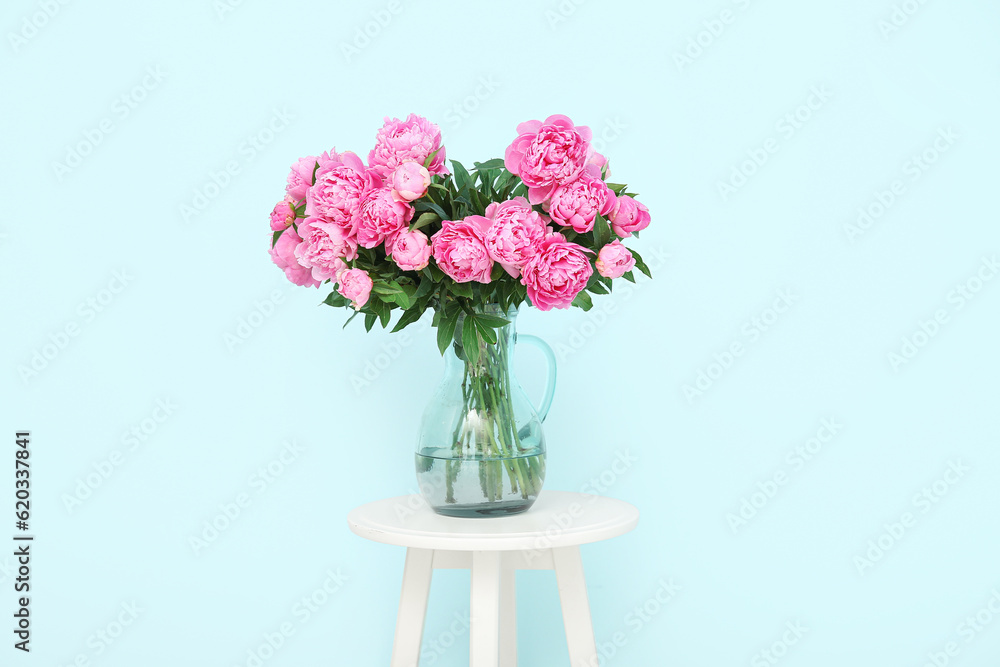 Vase of pink peonies on chair near blue wall